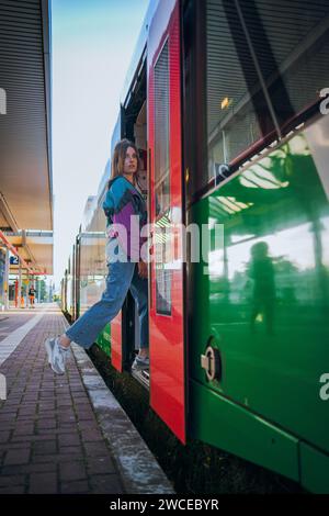 Kaukasisch aussehendes Mädchen, das in letzter Minute vor der Abfahrt in den Zug springt. Wunderschönes Mädchen posiert an einem sonnigen Sommertag vor der Tür des Zuges Stockfoto