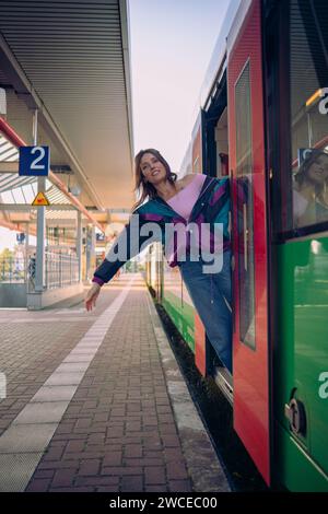 Kaukasisch aussehendes Mädchen, das in letzter Minute vor der Abfahrt in den Zug springt. Wunderschönes Mädchen posiert an einem sonnigen Sommertag vor der Tür des Zuges Stockfoto