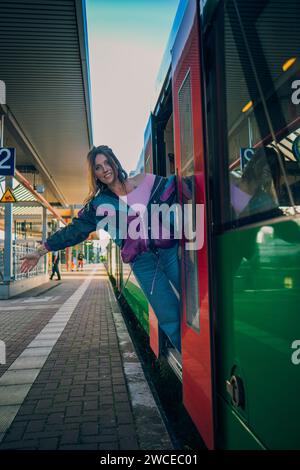 Kaukasisch aussehendes Mädchen, das in letzter Minute vor der Abfahrt in den Zug springt. Wunderschönes Mädchen posiert an einem sonnigen Sommertag vor der Tür des Zuges Stockfoto