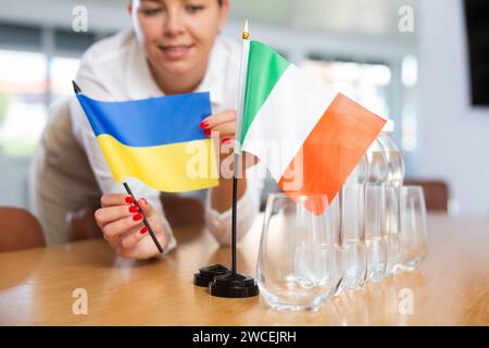 Vorbereitung auf Geschäftsverhandlungen - Frau setzt kleine Flaggen von Ländern der Ukraine und Italiens auf den Tisch Stockfoto