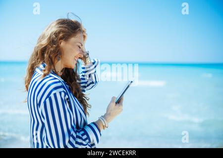 Glückliche elegante 40-jährige Frau an der Küste mit Smartphone. Stockfoto