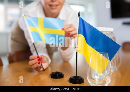 Weibliche Bürokoordinatorin, die Flaggen der Ukraine und Schwedens auf den Tisch setzt Stockfoto