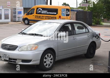 Gas wird in einen silbernen 2004 Toyota Corolla mit einer fehlenden Radkappe gepumpt Stockfoto