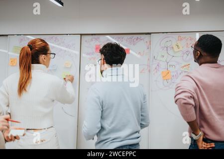 Geschäftskollegen arbeiten zusammen und entwickeln neue Ideen in einem Unternehmensbüro. Die Glaswand mit Haftnotizen spiegelt innovative Teamarbeit wider. Stockfoto