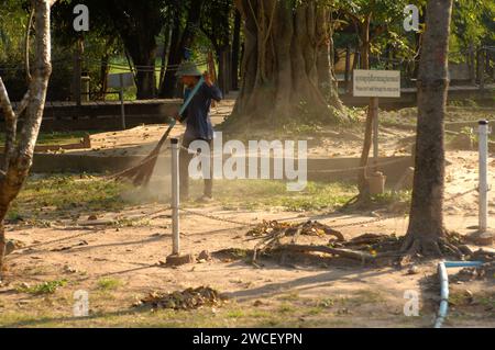 Damen fegen Blätter um einen Killing Tree in den Killing Fields des Choung EK Genocidal Center, Phnom Penh, Kambodscha. Stockfoto