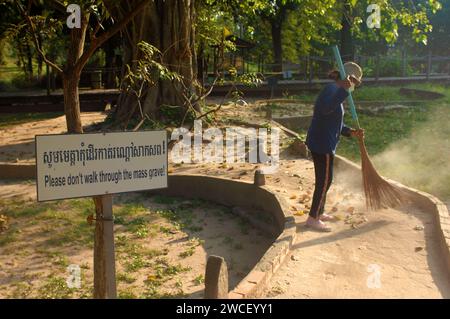 Damen fegen Blätter um einen Killing Tree in den Killing Fields des Choung EK Genocidal Center, Phnom Penh, Kambodscha. Stockfoto