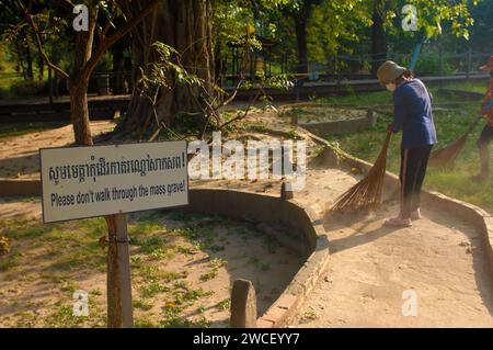 Damen fegen Blätter um einen Killing Tree in den Killing Fields des Choung EK Genocidal Center, Phnom Penh, Kambodscha. Stockfoto