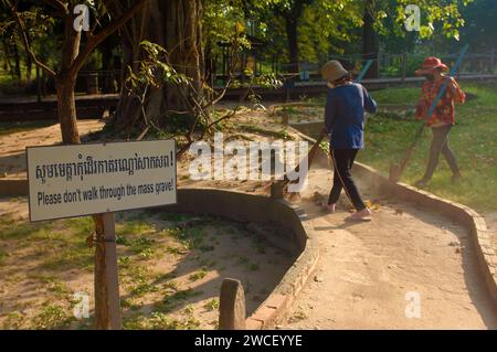 Damen fegen Blätter um einen Killing Tree in den Killing Fields des Choung EK Genocidal Center, Phnom Penh, Kambodscha. Stockfoto