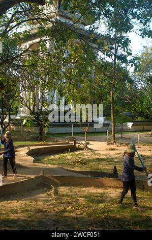 Damen fegen Blätter um einen Killing Tree in den Killing Fields des Choung EK Genocidal Center, Phnom Penh, Kambodscha. Stockfoto