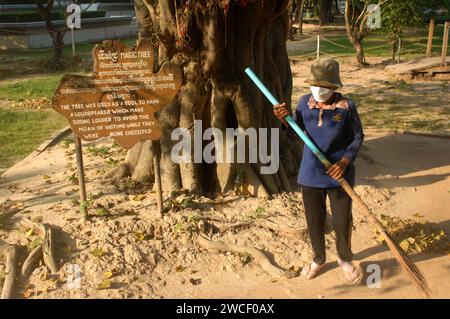 Damen fegen Blätter um einen Killing Tree in den Killing Fields des Choung EK Genocidal Center, Phnom Penh, Kambodscha. Stockfoto