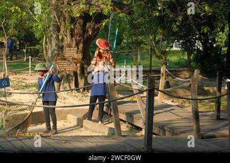 Damen fegen Blätter um einen Killing Tree in den Killing Fields des Choung EK Genocidal Center, Phnom Penh, Kambodscha. Stockfoto