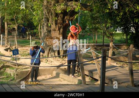 Damen fegen Blätter um einen Killing Tree in den Killing Fields des Choung EK Genocidal Center, Phnom Penh, Kambodscha. Stockfoto