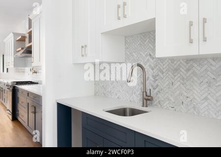 Ein Geschirr- oder Butler-Pantry-Detail mit Bronze-Armatur und Beschlägen, blau-weißen Schränken, Marmorfliesen mit Fischgrätmuster und Arbeitsplatte Stockfoto