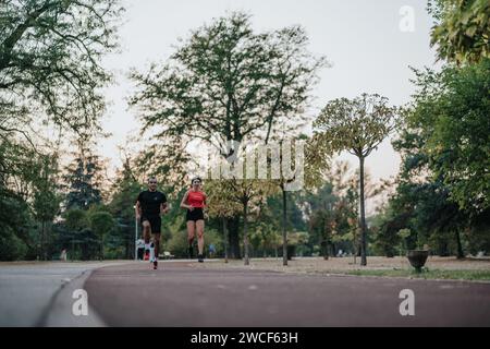 Zwei fitte Läufer, ein Mann und eine Frau, joggen in einem Park in der Abenddämmerung. Stockfoto