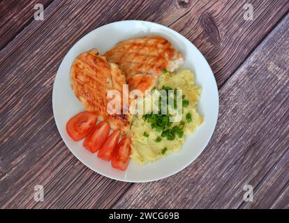 Zwei Stücke gegrilltes Hähnchenfilet mit Kartoffelpüree und Tomatenscheiben auf einem Holztisch. Draufsicht, flach. Stockfoto