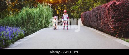 Zwei kleine Mädchen fahren auf Rollern und Laufrädern im Sommerpark. Kinder tragen Schutzpolster und Schutzhelm für eine sichere Fahrt. Aktiver Outdoor-Sport f Stockfoto