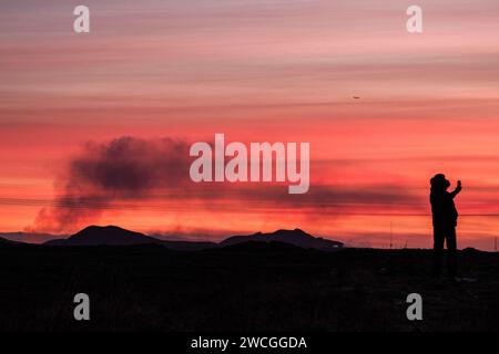 Grindavik, Island. Januar 2024. Ein Tourist lässt sich ein Foto mit dem Vulkanausbruch im Hintergrund machen. Seit der Vulkanausbruch am Morgen des 14. Januar begann, ist die Intensität der Eruption rückläufig, obwohl einige Häuser von Lava getroffen wurden. Notfallteams und Polizei halten die Situation unter Kontrolle, um sicherzustellen, dass es keine größeren Zwischenfälle gibt. (Foto: Raul Moreno/SOPA Images/SIPA USA) Credit: SIPA USA/Alamy Live News Stockfoto