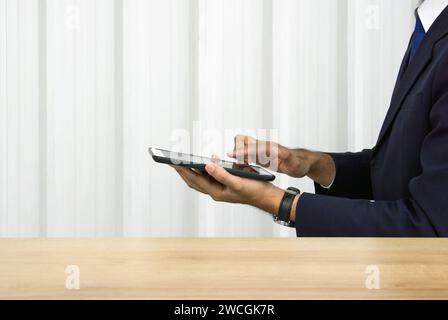 Ein fokussierter Geschäftsmann im dunkelblauen Anzug, der auf einem Tablet-Computer schreibt. Seitenansicht. Digitale Lebensforschung. Stockfoto