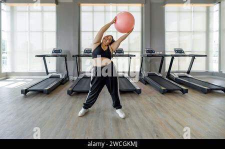 Eine Frau ist in einem Fitnessstudio und packt mit beiden Händen einen rosa Ball, bereit zum Training. Stockfoto