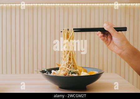 Hand nimmt Yaki Ramen mit schwarzen Essstäbchen für das Essen im japanischen Restaurant. Bokeh-Hintergrund. Authentische und traditionelle japanische Nudeln. Stockfoto