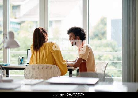 Fröhliche Kollegen sitzen am Schreibtisch und genießen es, gemeinsam an Projekten zu arbeiten Stockfoto