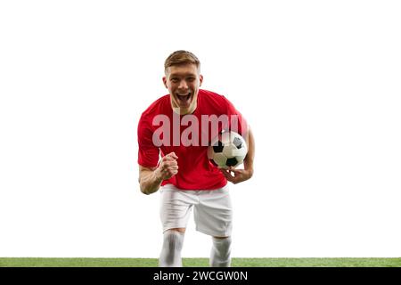 Siegesstarre. Der gewinnende Geist des Fußballspielers, der Ball hält, der Blick auf die Kamera gerichtet, die Faust im Triumph geballt, steht auf dem Spielplatz gegen weiß Stockfoto