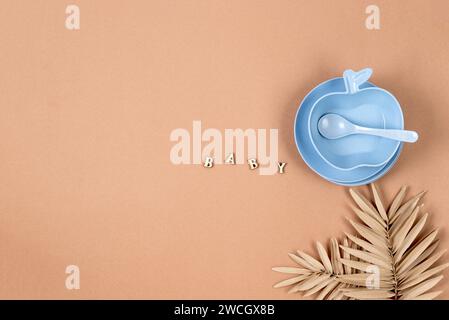 Babytisch-Einstellung. Silikon-Set mit blauem Teller, Tasse, Besteck auf pastellbeigem Hintergrund. Platz für Text, Kopierraum. Stockfoto