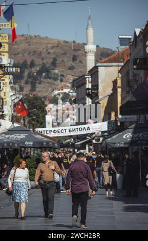 Shirok Sokak Straße im Zentrum von Bitola, Nordmazedonien. An einem sonnigen Tag laufen die Menschen die Straße entlang, mit dem Minarett einer Moschee hinten. Stockfoto