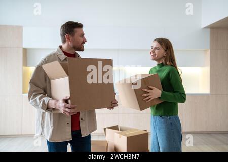 Glückliche neue Hausbesitzer Mieter, junge Paare, zufriedener Mann und freudige Frau, die Kisten ins Zimmer tragen Stockfoto