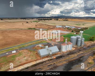 Aus der Vogelperspektive auf Getreidesillos entlang einer ländlichen Eisenbahnlinie mit dunklen Wolken und Regen in der Ferne bei Moolort in Central Victoria, Australien. Stockfoto