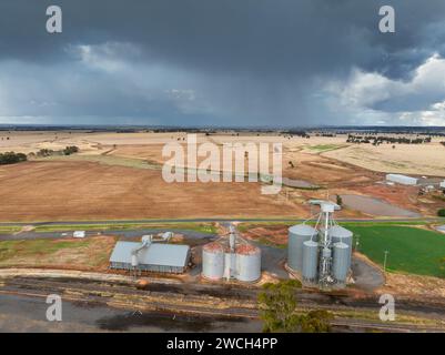 Aus der Vogelperspektive auf Getreidesillos entlang einer ländlichen Eisenbahnlinie mit dunklen Wolken und Regen in der Ferne bei Moolort in Central Victoria, Australien. Stockfoto