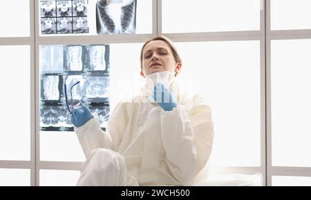 Müde Arzt in Schutzanzug sitzt auf dem Boden mit Röntgenstrahlen Hängend im Hintergrund Stockfoto