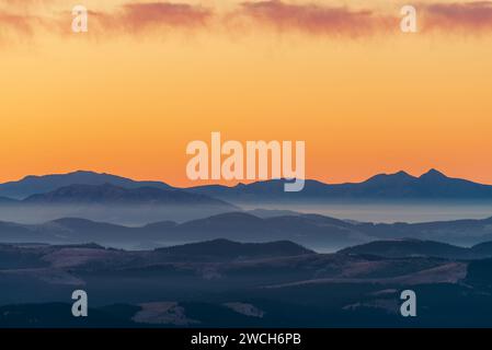 Ein außergewöhnlicher Blick auf die Berge, die mit Schnee und Nebel bedeckt sind, vor dem orangefarbenen Himmel. Ein Konzert der Freiheit und der Schönheit der Natur. Stockfoto