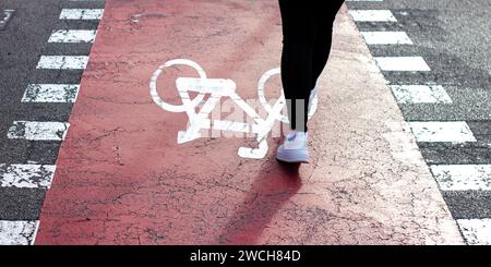 Das Mädchen in weißen Sneakers mit einer Jeansjacke geht zu Fuß über einen Fahrradweg. Fahrradschild auf Asphalt gemalt. Stockfoto