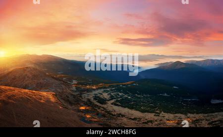 Sonnenuntergangspanorama in einem Bergtal mit niedrigen Wolken. Dramatische Landschaft mit Sonnenuntergang Himmel, Bergen und Nebel. Stockfoto