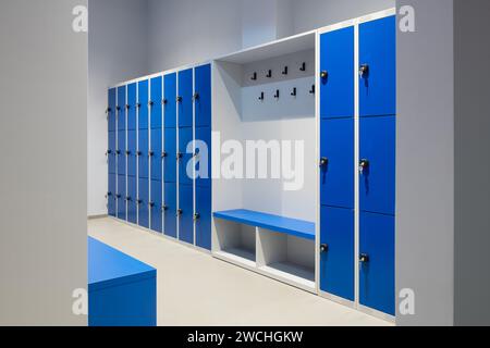 Eine Reihe blauer Schließfächer an einer Wand mit Schlüssel in einem Schloss und einer Bank Stockfoto