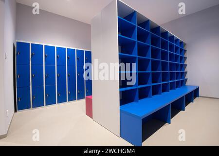 Blaue Schließfächer an der Wand und Schrank mit leeren Regalen mit Bank davor Stockfoto