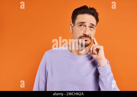 Bärtiger Mann in lila Pullover und Jeans, der an Zahnschmerzen auf orangefarbenem Hintergrund leidet, Schmerzen Stockfoto