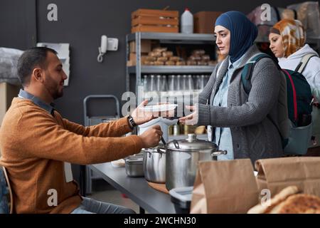 Seitenansicht Porträt einer Frau aus dem Nahen Osten, die Hijab trägt und in der Suppenküche oder im Flüchtlingshilfezentrum warme Mahlzeiten erhält Stockfoto