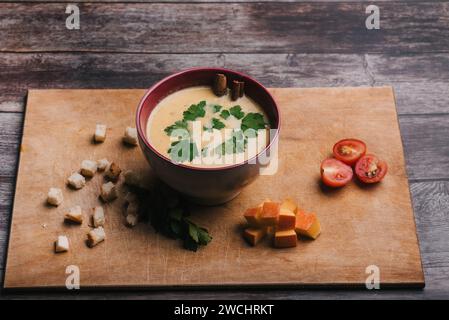 Kürbiscremesuppe in einer Schüssel mit Petersilie auf einem Holztisch mit Crackern und Tomaten. Traditionelle vegetarische Herbstdiät für Halloween Stockfoto