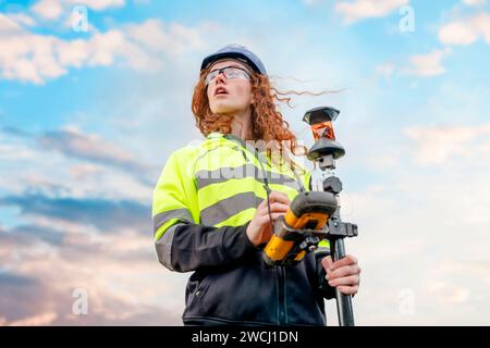 Weibliche Landvermessungsfrau, die mit Modern arbeitet, die geodätische Instrumententachometer prüfen, Koordinaten von Land für Entwicklung. Junge hübsche Frau Stockfoto