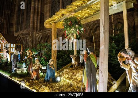 Eine heitere Krippe taucht in das sanfte Licht der Dämmerung, vor der historischen Kulisse von Notre-Dame de Straßburg und fängt das Wesen des Weihnachtsfests im Elsass ein. Stockfoto