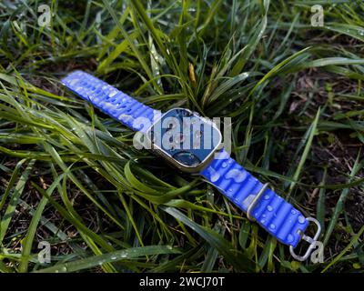 Paris, Frankreich - 23. September 2022: Das Bild zeigt eine verlorene Apple Watch Ultra 2, die auf nassgrünem Gras liegt und die wasserabweisenden Eigenschaften der Uhren nach einem Regenfall zeigt – blaues Armband Stockfoto