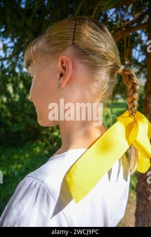7-jähriges Mädchen in einem Kostüm und geflochtenem Zopf mit gelber Schleife, fotografiert vom Profil. Stockfoto