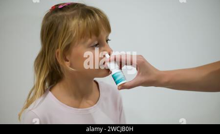 Mutter sprüht Nasenspray gegen das Fieber ihrer Tochter, das kleine Mädchen wird zu Hause behandelt und ist im Pyjama - verschwommener Hintergrund. Stockfoto