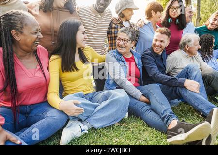 Gruppe von Menschen aus mehreren Generationen, die zusammen lächeln und lachen - multirassische Freunde mit verschiedenen Altern, die Spaß im Freien im Stadtpark haben - Hauptfokus Stockfoto