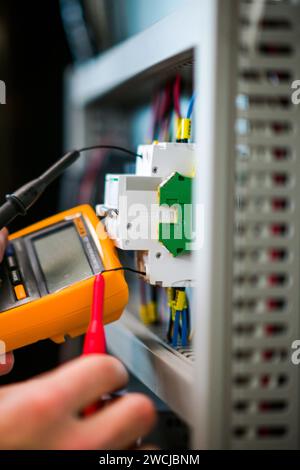 Ein Elektriker, der in einem Schaltschrank arbeitet, prüft Kabel mit einem Tester. Stockfoto