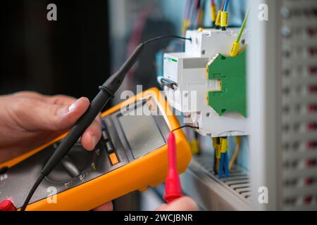 Ein Elektriker, der in einem Schaltschrank arbeitet, prüft Kabel mit einem Tester. Stockfoto