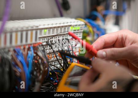 Ein Elektriker, der in einem Schaltschrank arbeitet, prüft Kabel mit einem Tester. Stockfoto