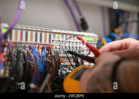 Ein Elektriker, der in einem Schaltschrank arbeitet, prüft Kabel mit einem Tester. Stockfoto